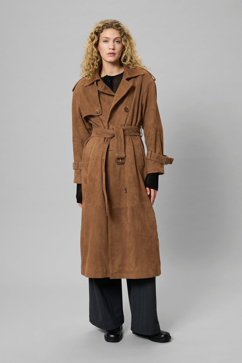 Kvinde iført cognacfarvet trenchcoat med bælte, epauletter og dobbeltknappet front.