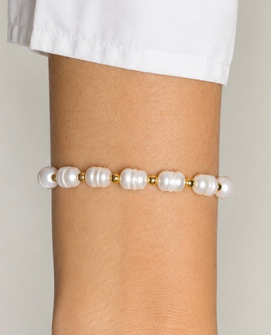 Armbånd fra Andcopenhagen Jewelry i 18 karat guldbelagt messing med hvide perler på en arm.