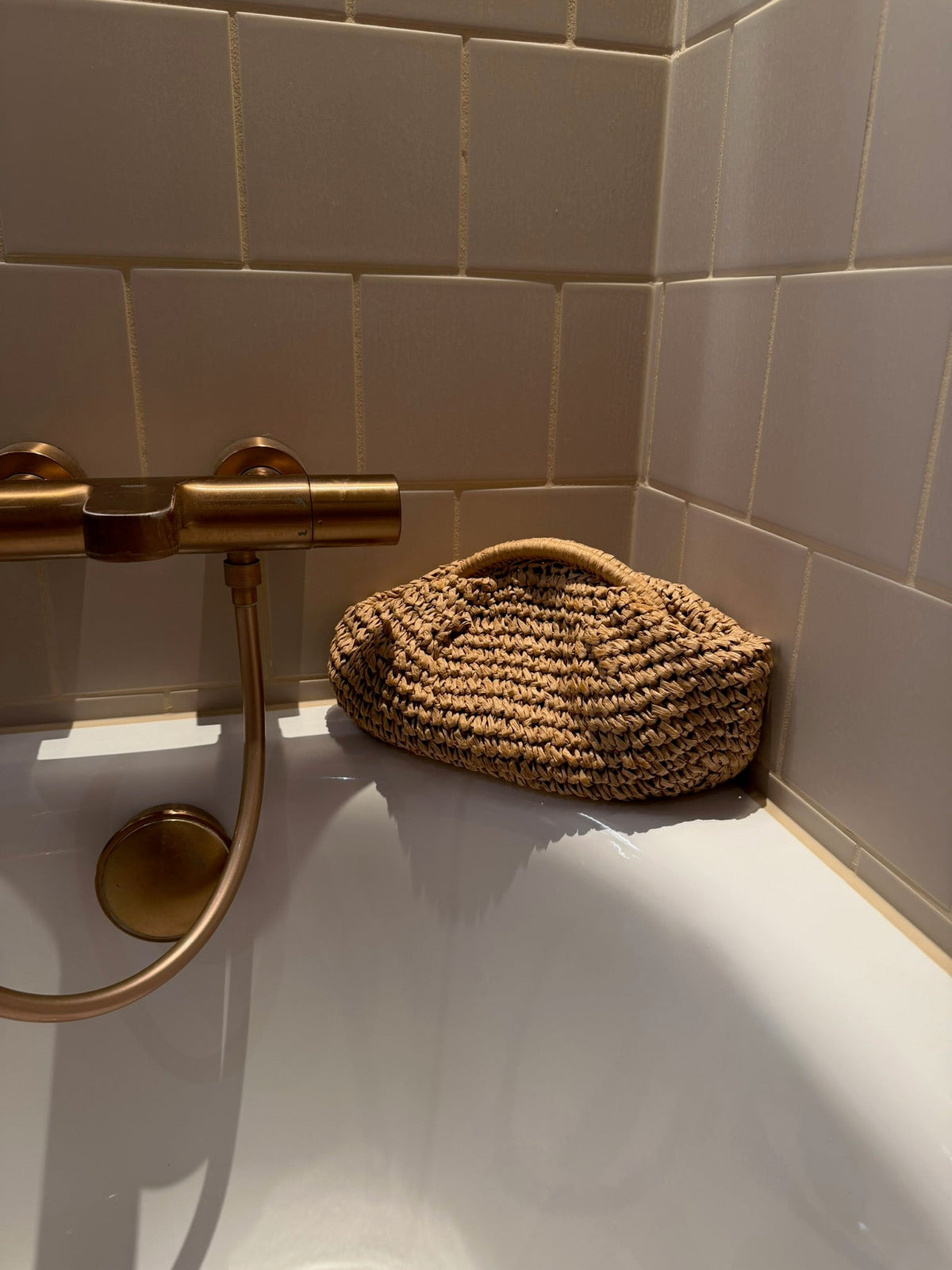 Andcopenhagen Basics stråtaske i khaki farve placeret på kanten af et badekar med beige fliser.