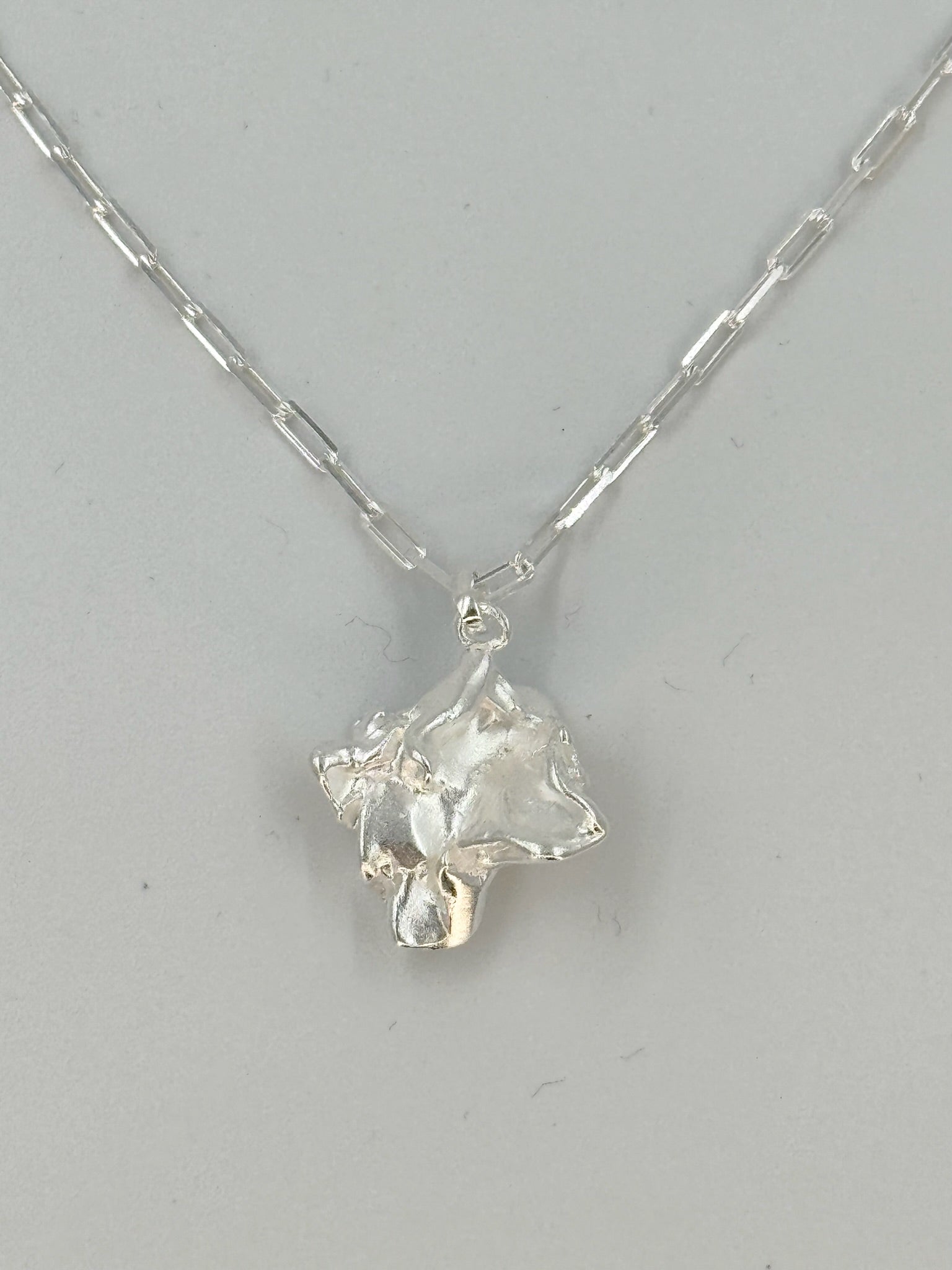 Sølvhalskæde med flade led og skulpturelt, organisk vedhæng.