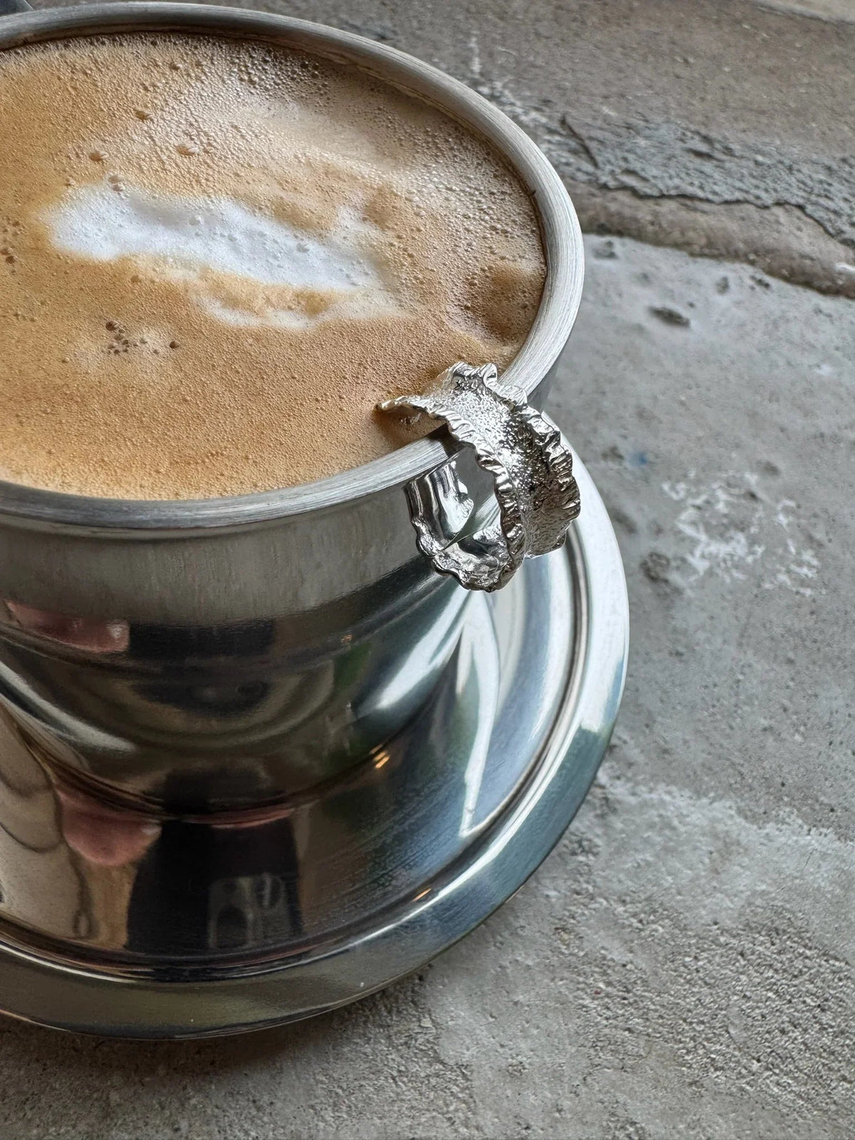 Sandy ring i 925 sterlingsølv fra Andcopenhagen vises på kanten af en sølvkop med kaffe.