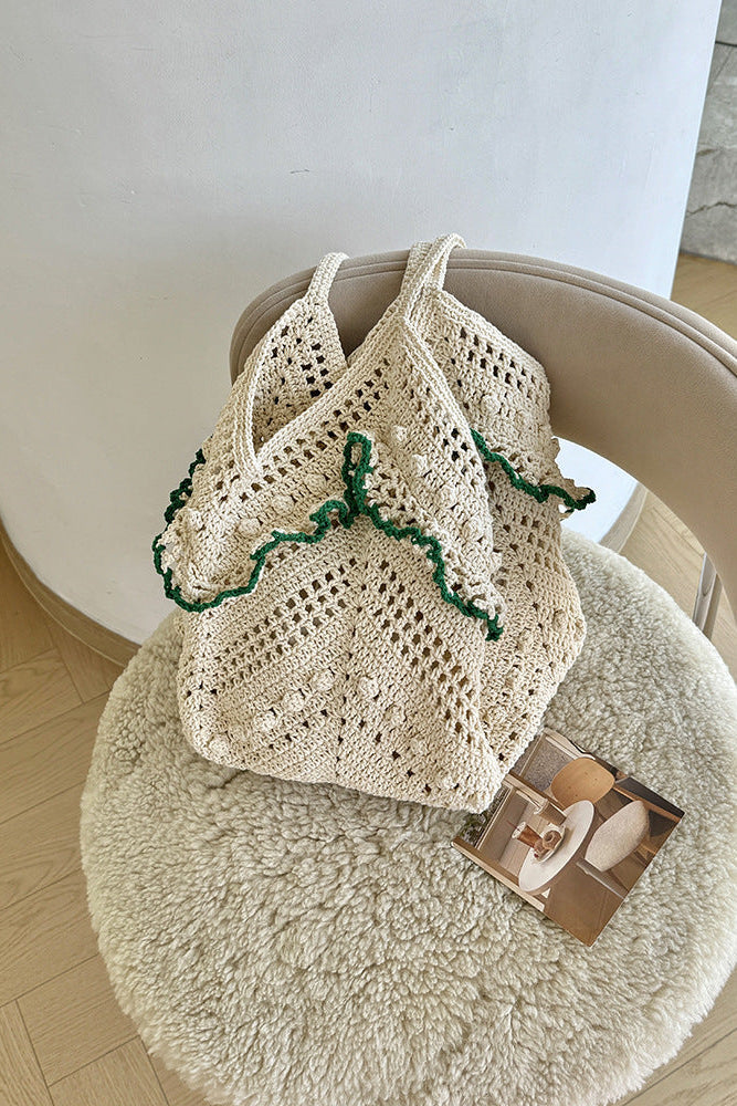 Andcopenhagen Basics Ginny taske i creme med grønne detaljer, vist på en blød stol.