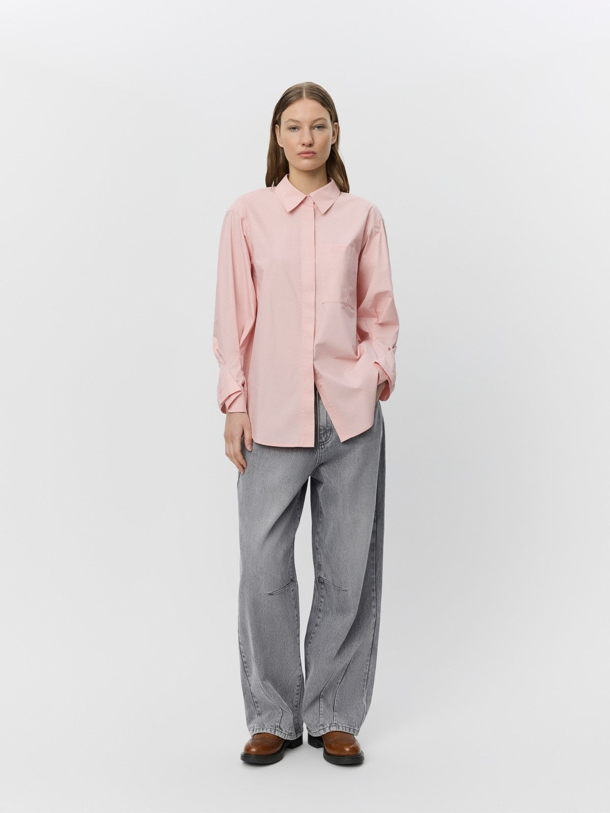 Lys pink skjorte med klassisk krave, brystlomme, rynkede manchetter, grå jeans og brune sko.