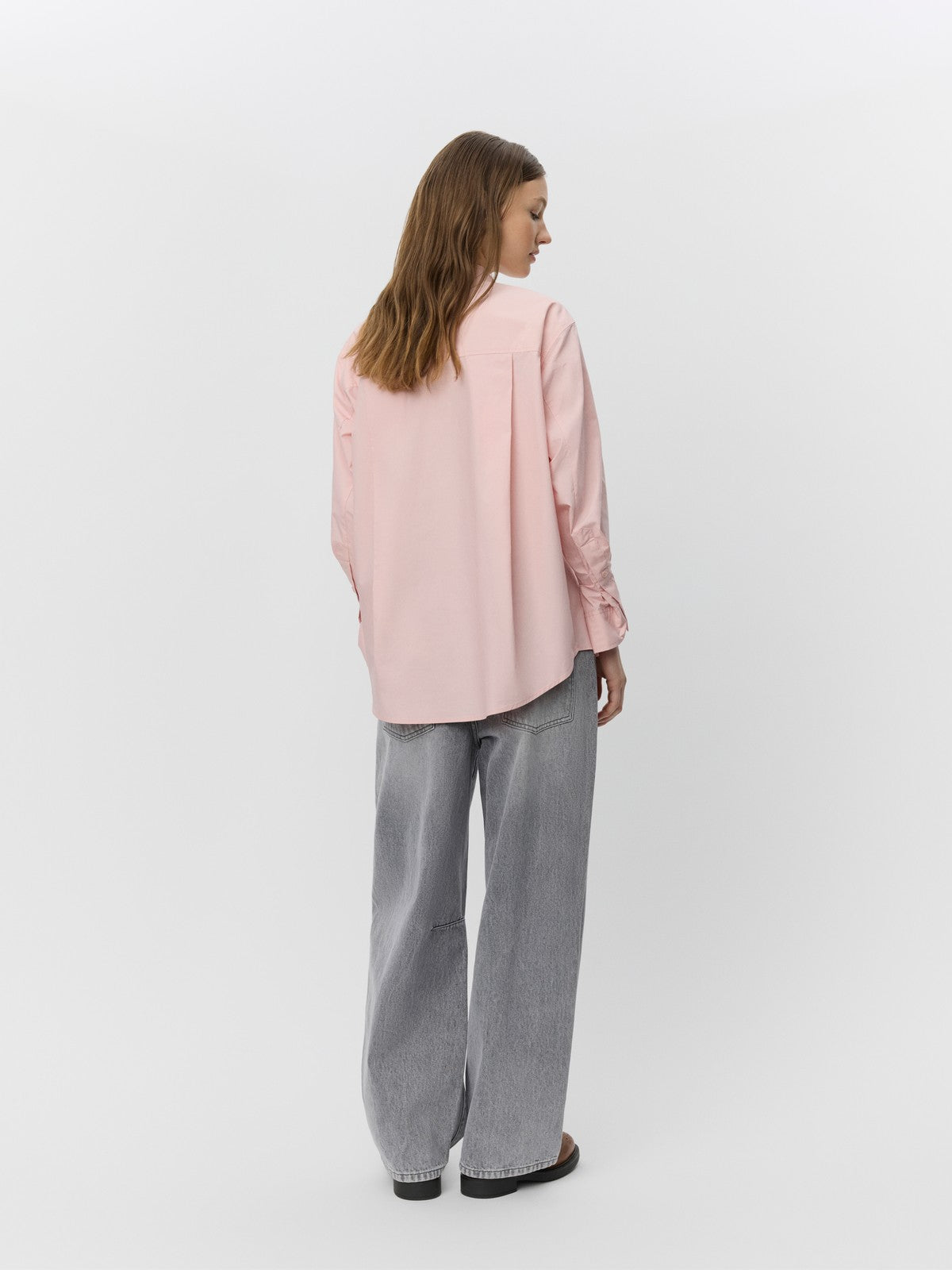 Kvinde set bagfra i lys pink skjorte med klassisk krave og grå vide jeans.