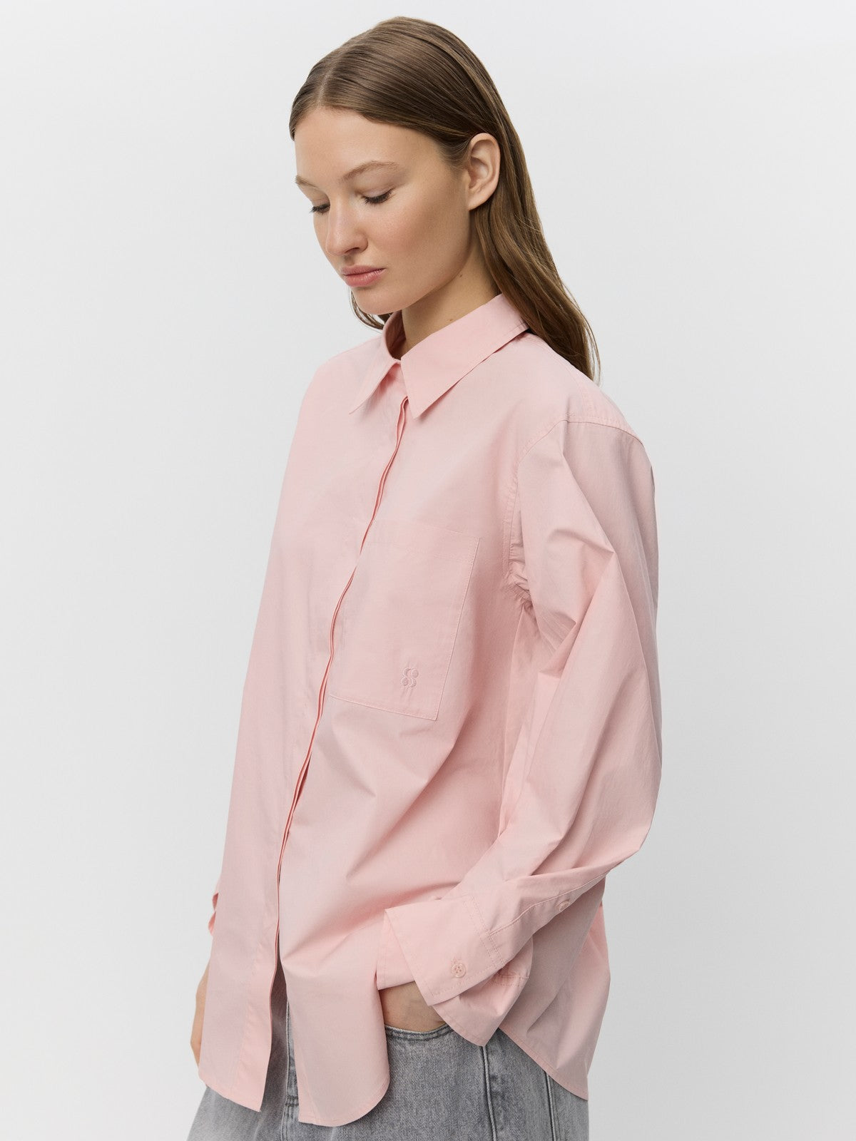 Lys pink skjorte med krave, brystlomme og rynkede manchetter, båret af person med langt hår.