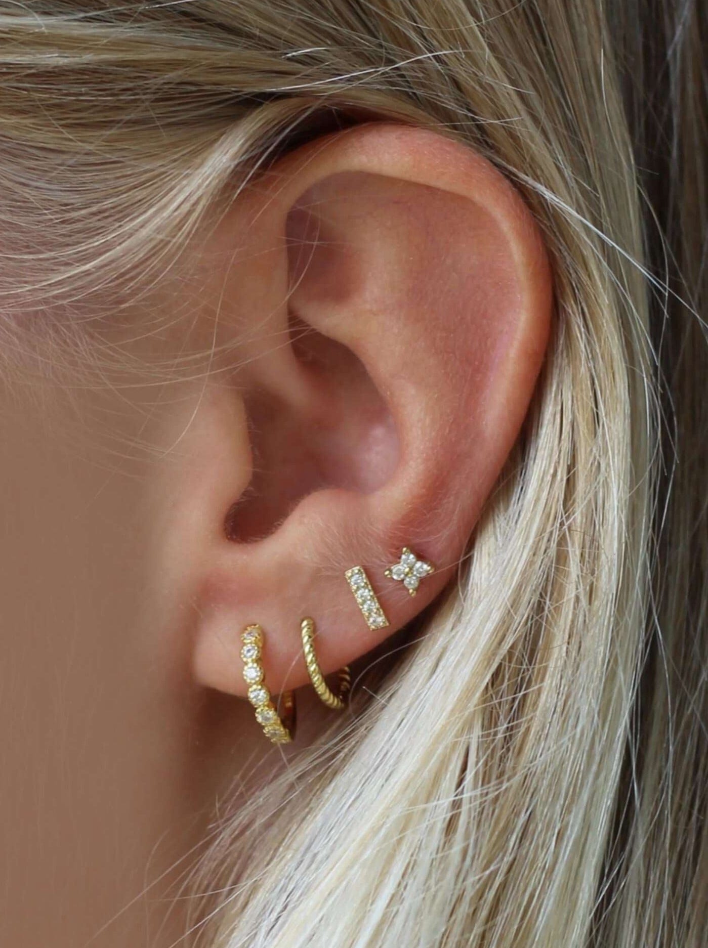 Fire øreringe i øret, guldbelagte med sten, inkl. hoops og stænger, på en lys hudtone.