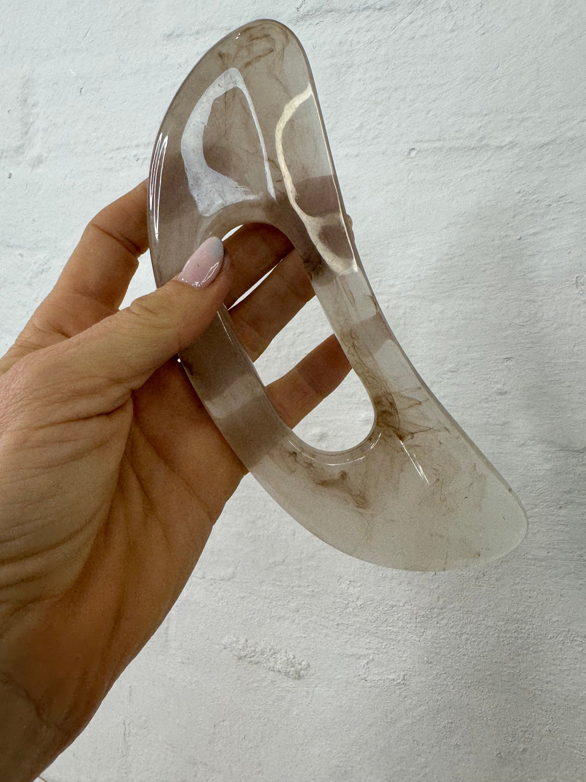 Gennemsigtigt gua sha værktøj fra Andcopenhagen Basics holdes i hånd, til kropsmassage.
