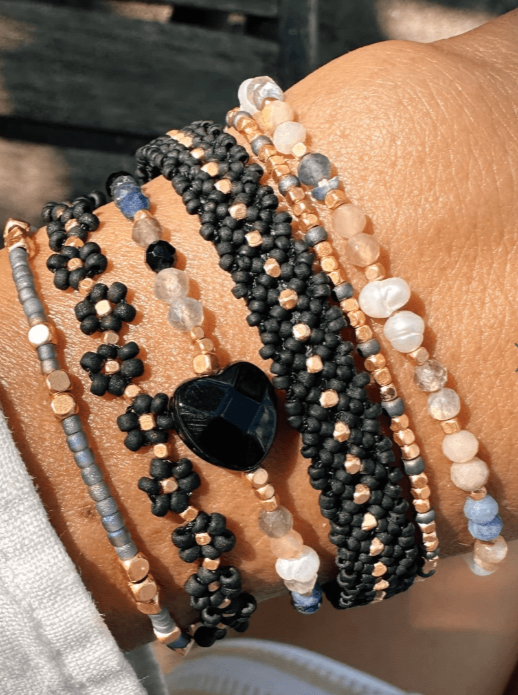 Sort armbånd med guldperler, båret med flere farverige perlearmbånd, inkl. blomster- og hjerteform.