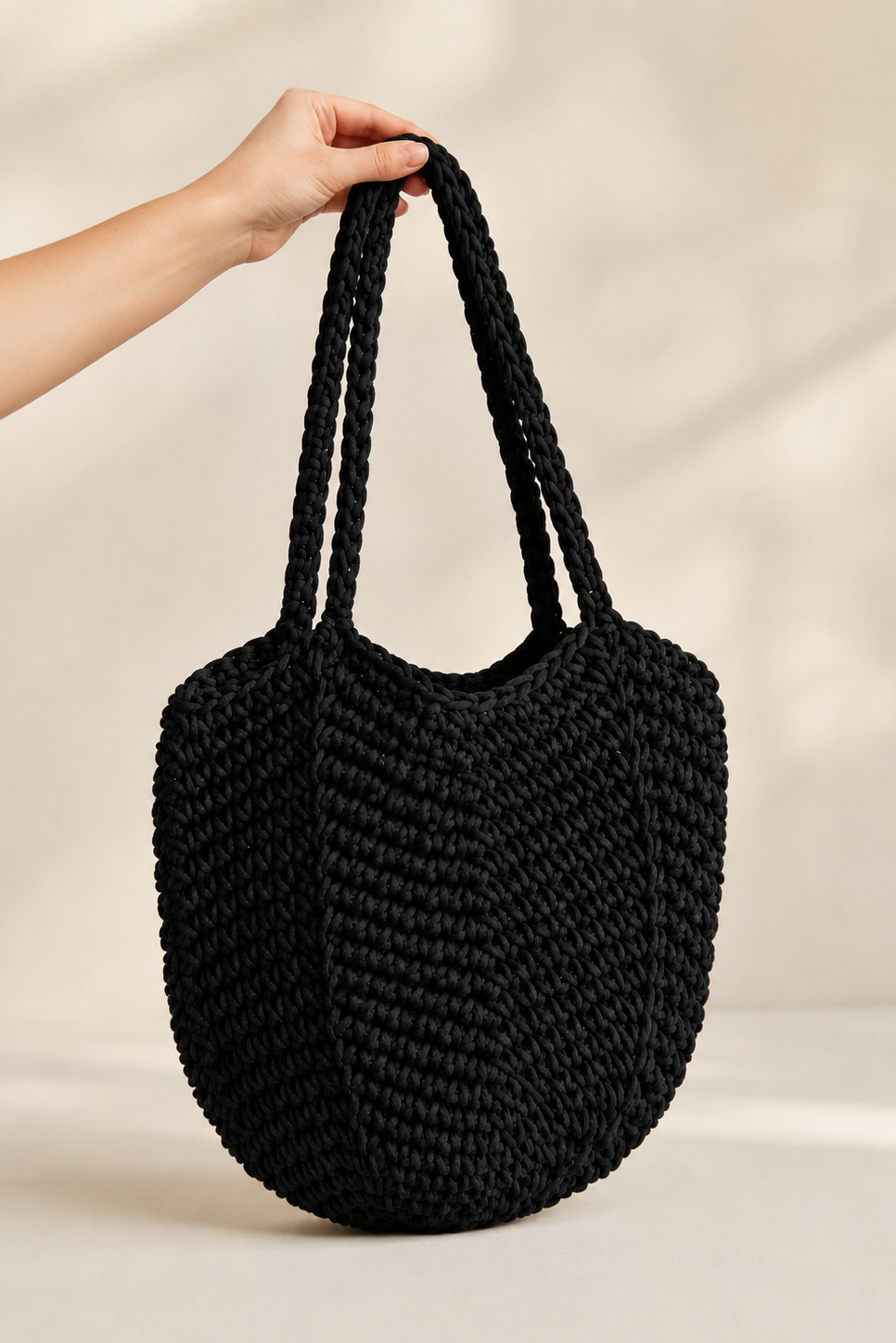 Sort Andcopenhagen Basics taske "Kelly" med flettet mønster, holdt i hånd mod neutral baggrund.