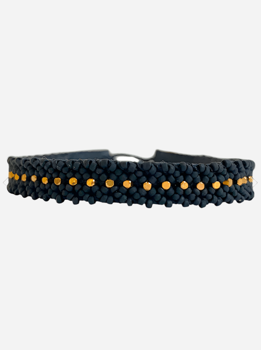 Sort flettet armbånd med små guldperler i midten og en synlig metallisk lukning.