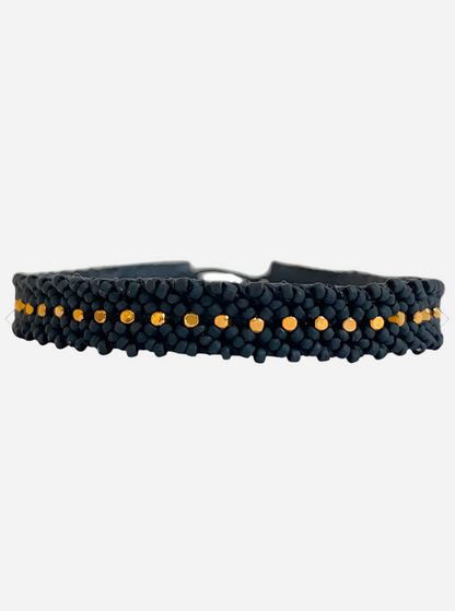 Sort flettet armbånd med små guldperler i midten og en synlig metallisk lukning.