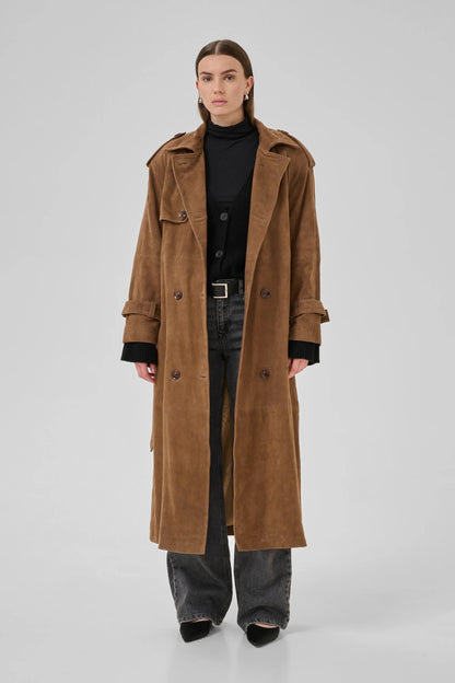 Person iført cognacfarvet trenchcoat med dobbeltknapper, epauletter og bælte over sort tøj.