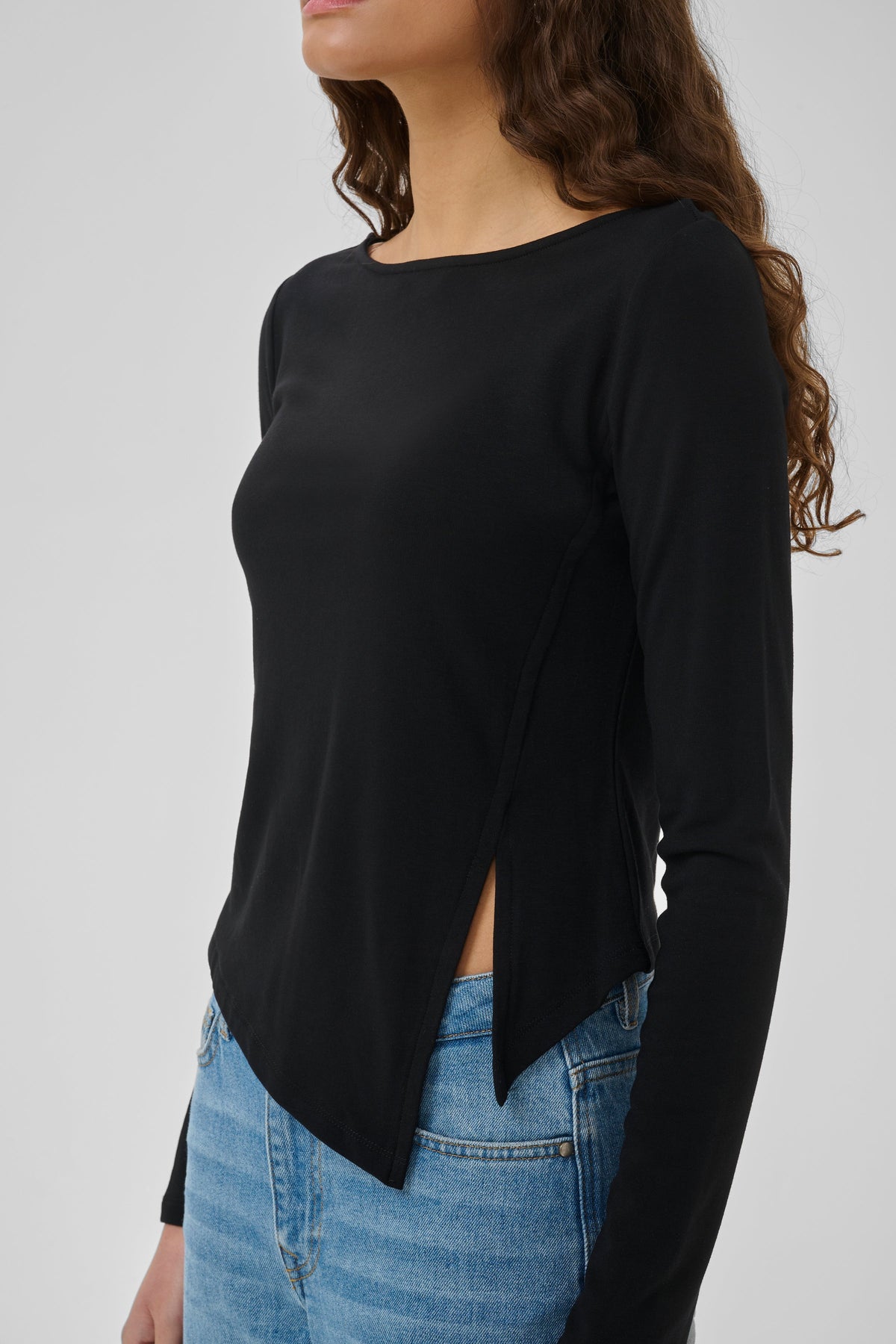 Nupti-blusen fra My Essential Wardrobe er en elegant, sort bluse med et moderne asymmetrisk snit på mørkhåret kvinde
