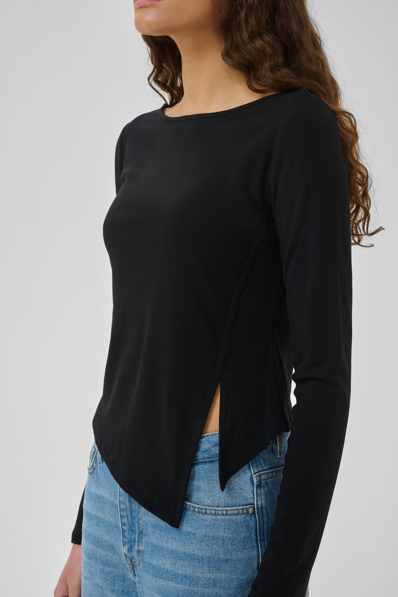 Nupti-blusen fra My Essential Wardrobe er en elegant, sort bluse med et moderne asymmetrisk snit på mørkhåret kvinde