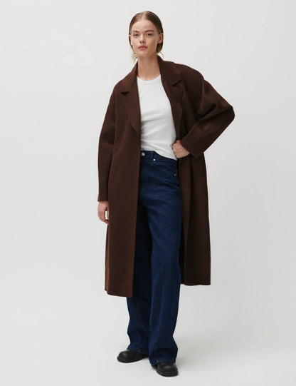 Mørkebrun frakke med reverskrave og bælte, bæres over hvid top og mørke jeans.