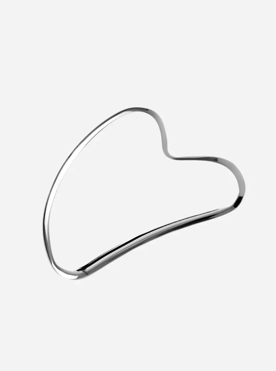 Gua sha værktøj i rustfrit stål med hjerteformet design og skinnende, glat overflade.