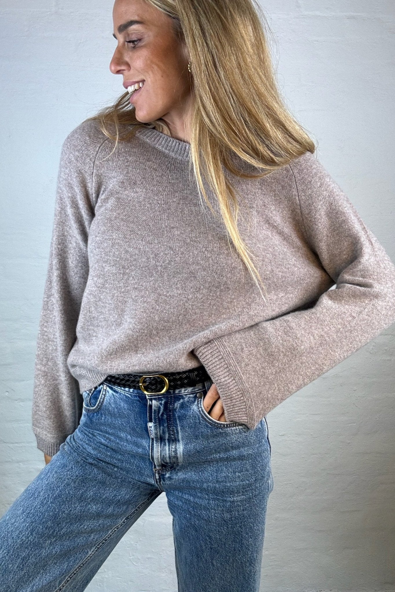 Kvinde i lys brun oversized cashmerebluse med rund hals, kombineret med jeans og bælte.