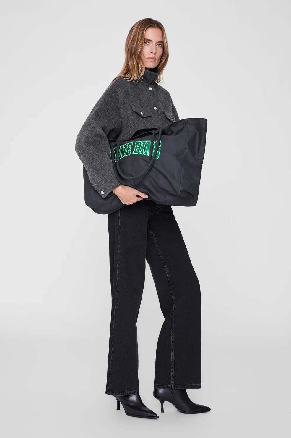 ANINE BING Leo Canvas Tote i vasket sort bomuldscanvas med grønne detaljer, broderet logo på fronten og lange skulderstropper som holdes af en kvinde