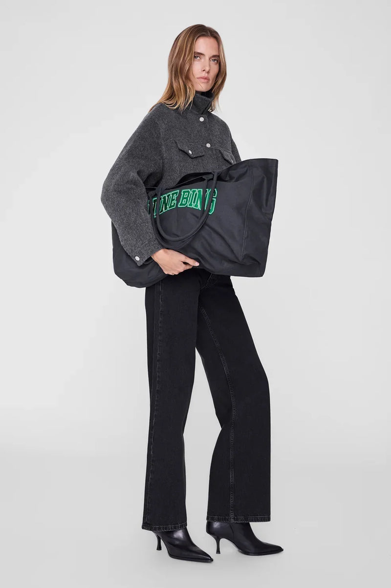 ANINE BING Leo Canvas Tote i vasket sort bomuldscanvas med grønne detaljer, broderet logo på fronten og lange skulderstropper som holdes af en kvinde
