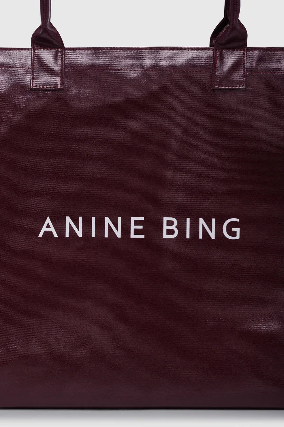 ANINE BING Leo Coated Canvas Tote i dyb bordeaux (Fig) med stort kontrastfarvet logo på fronten og lange skulderstropper tæt på