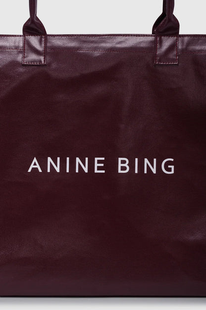 ANINE BING Leo Coated Canvas Tote i dyb bordeaux (Fig) med stort kontrastfarvet logo på fronten og lange skulderstropper tæt på