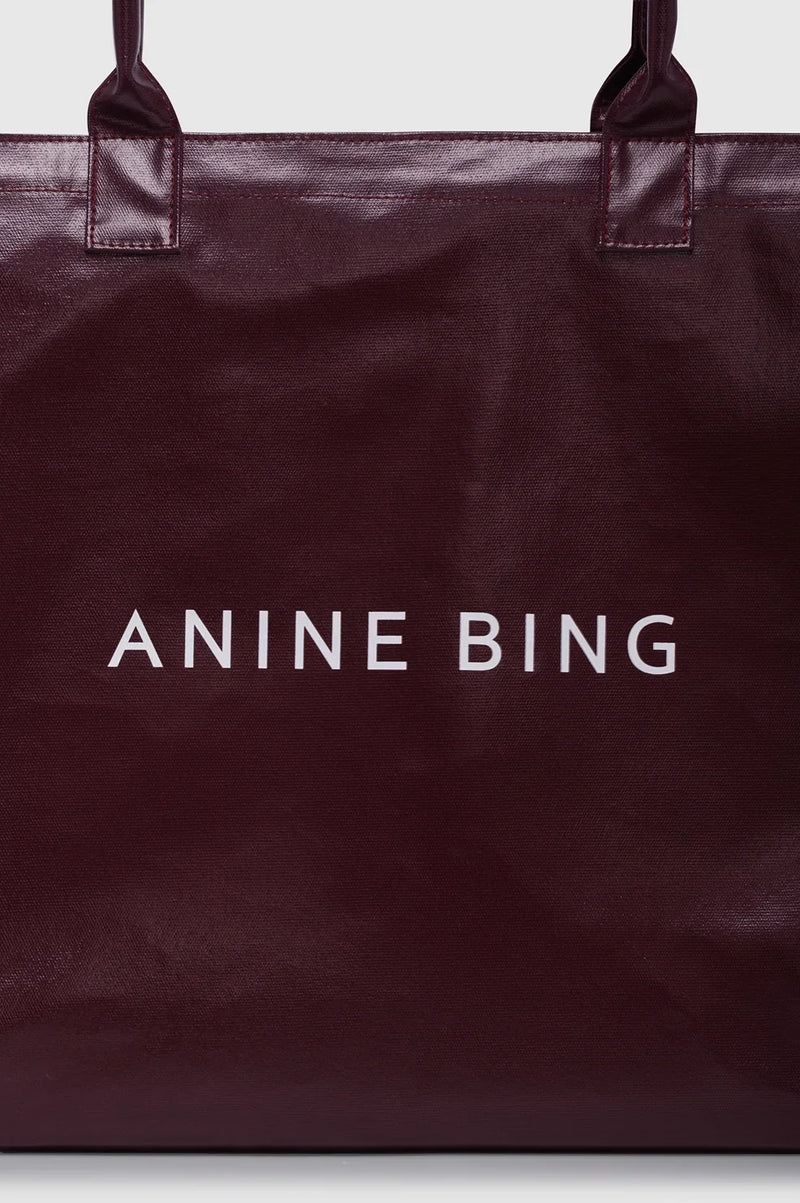 ANINE BING Leo Coated Canvas Tote i dyb bordeaux (Fig) med stort kontrastfarvet logo på fronten og lange skulderstropper tæt på