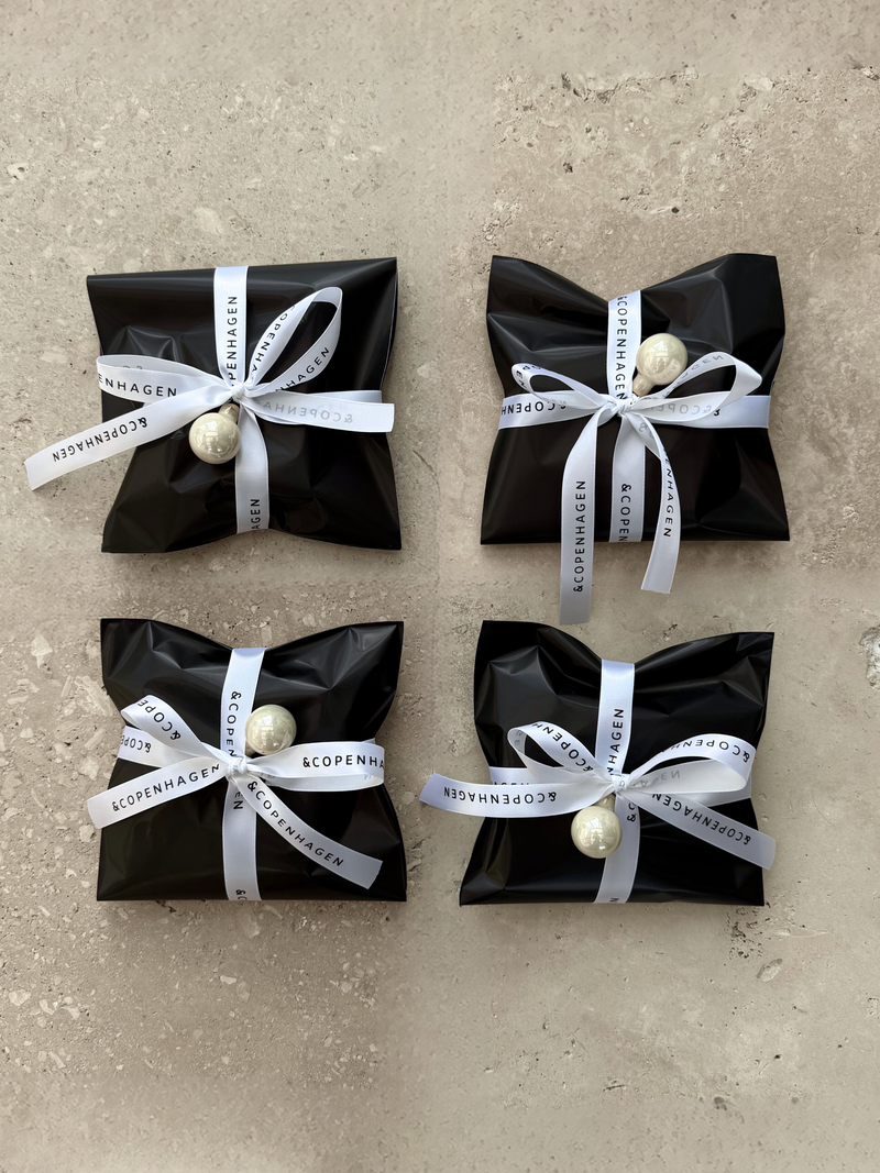 Fire sorte pakker med hvide bånd og perler, Andcopenhagen Jewelry Adventskalender på produktside.