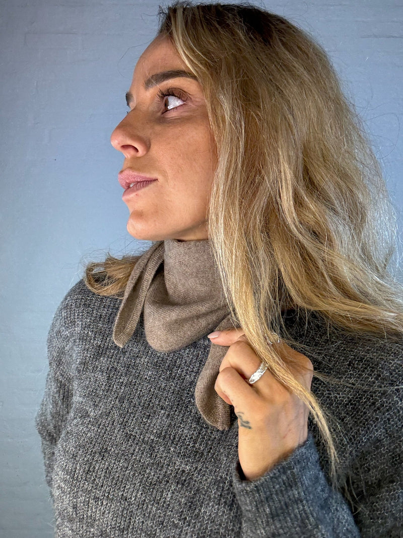 Model med mørkebrun cashmere mini tørklæde om halsen. Tørklædet er blødt og elegant.