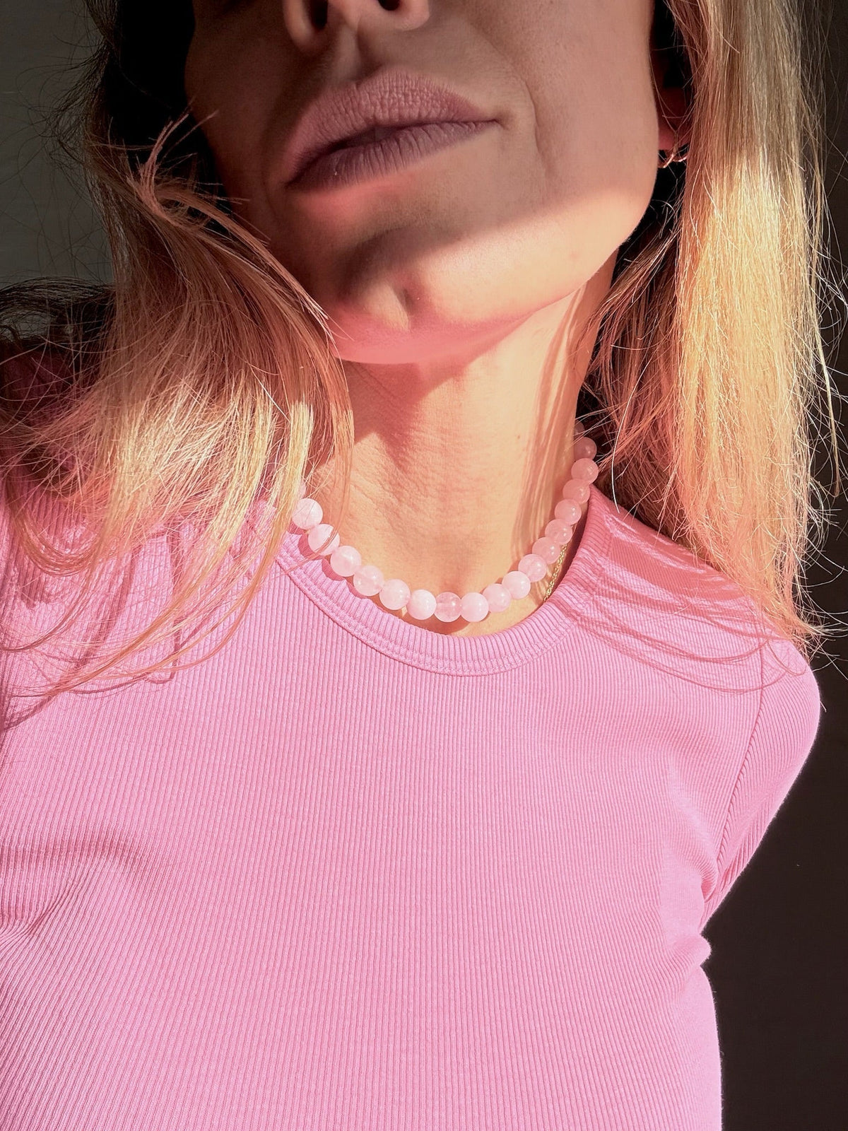 Kvinde med Andcopenhagen rosa kvarts halskæde, iført lyserød bluse, set tæt på.