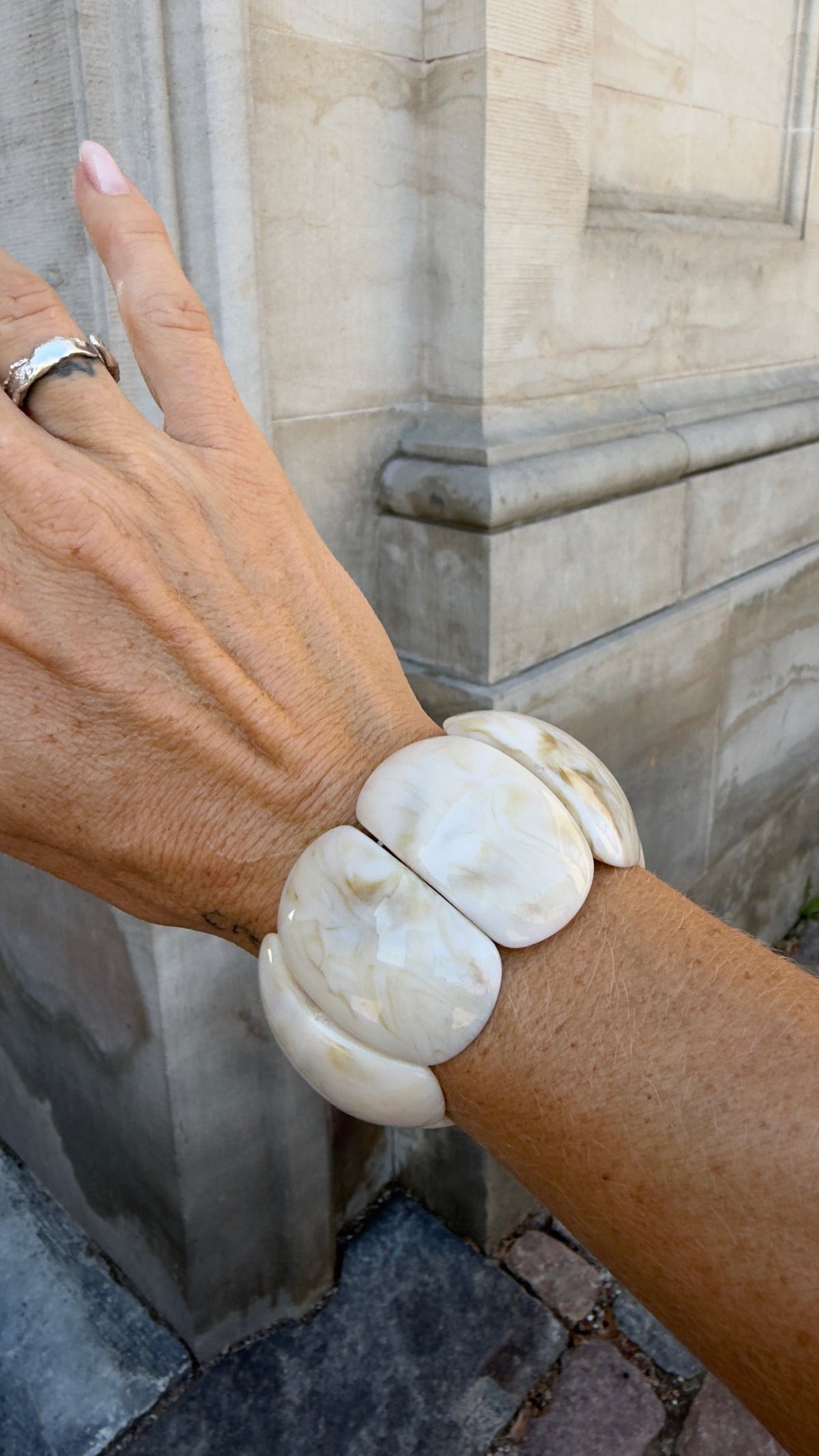 Armbånd fra Andcopenhagen Jewelry - Resin - Fraj Shell bæres på håndled mod lys murstensbaggrund.