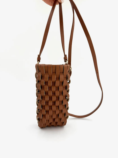 Cognacfarvet telefonetui med vævet design og lange stropper, holdt op mod en hvid baggrund.