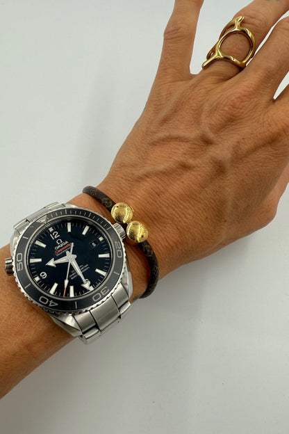 Hånd med Louis Vuitton armbånd, guldender med logo, og et ur. Armbåndet har et klassisk mønster.
