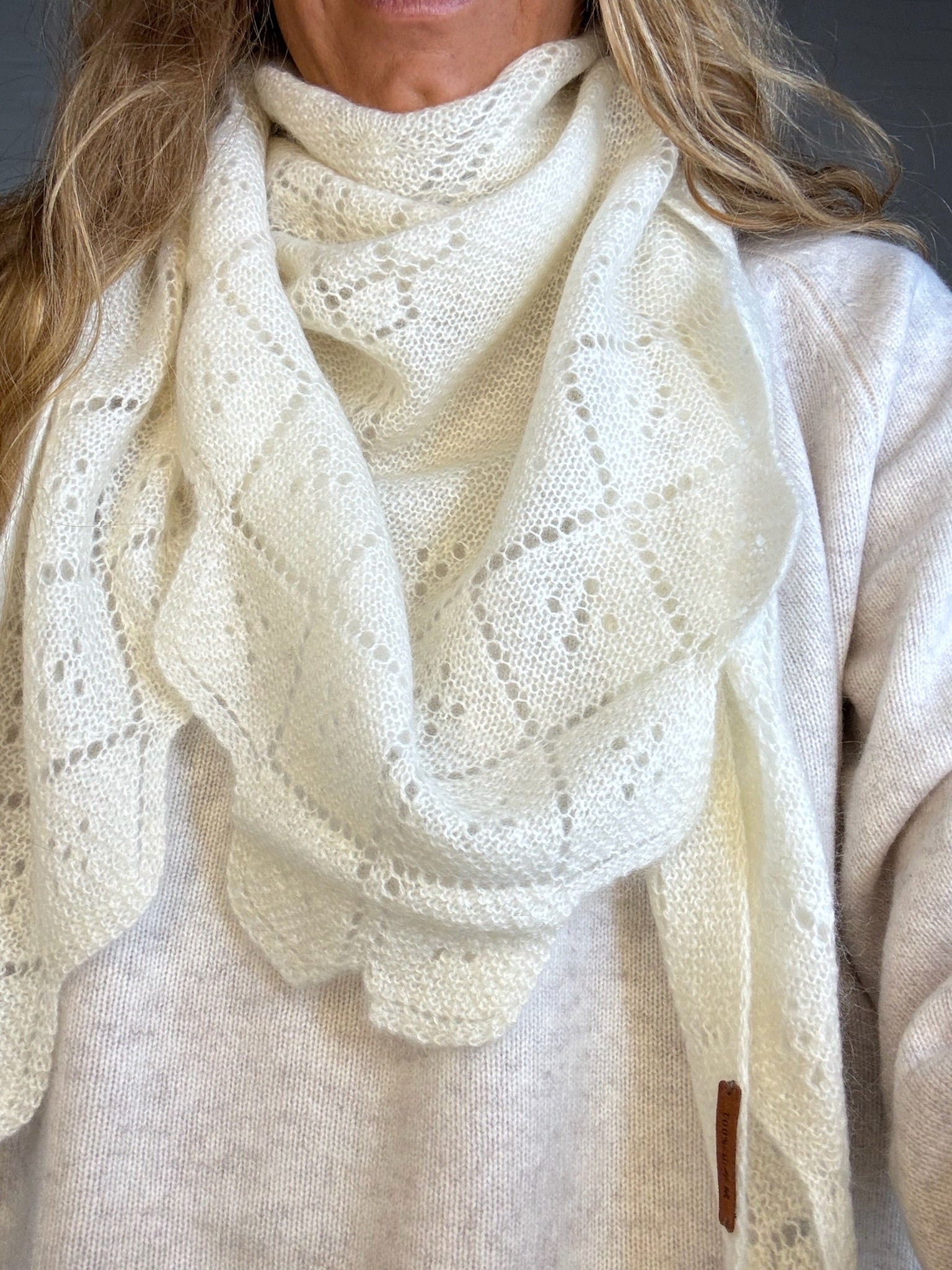 Hvidt cashmere tørklæde med geometrisk mønster og små huller, draperet om en persons hals.