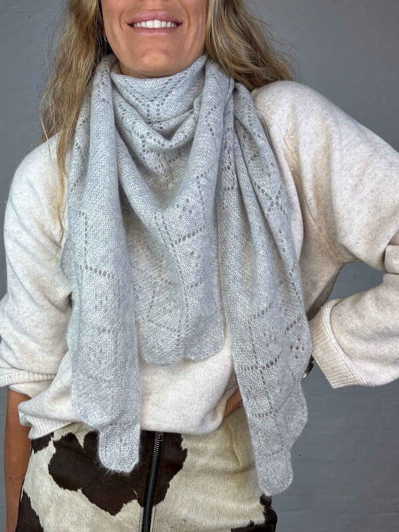 Gråt trekantet cashmere tørklæde med bladmønster, båret af person i lys trøje.