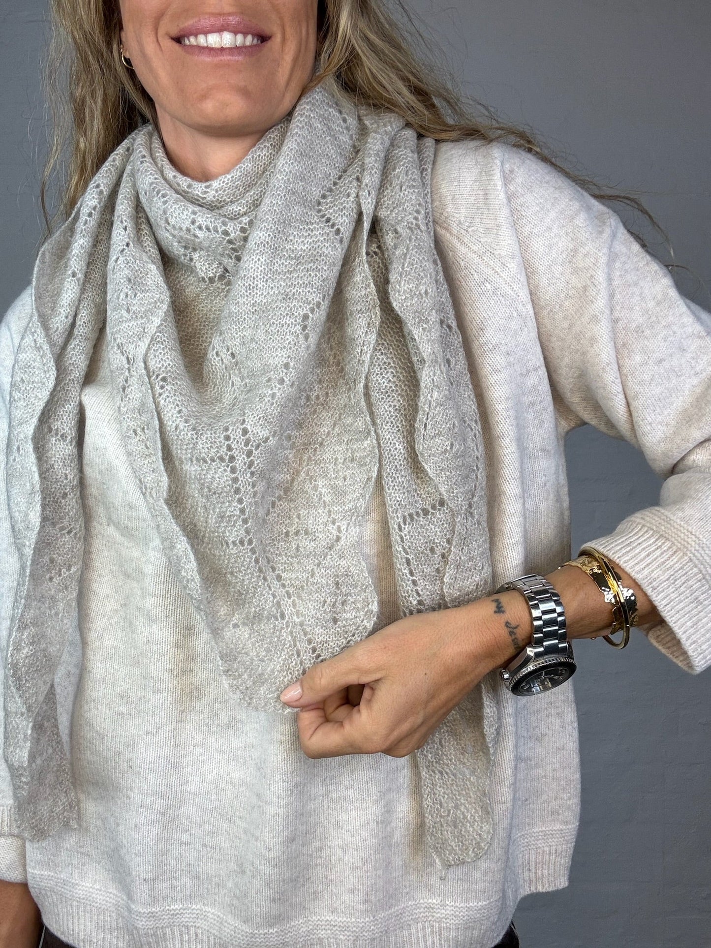 Person iført lys beige cashmere tørklæde over matchende sweater, justerer tørklædet.