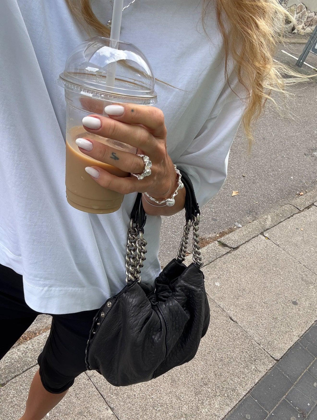 Kvinde med Arlinda armbånd i 925 sterlingsølv fra Andcopenhagen, holder iskaffe og sort taske.