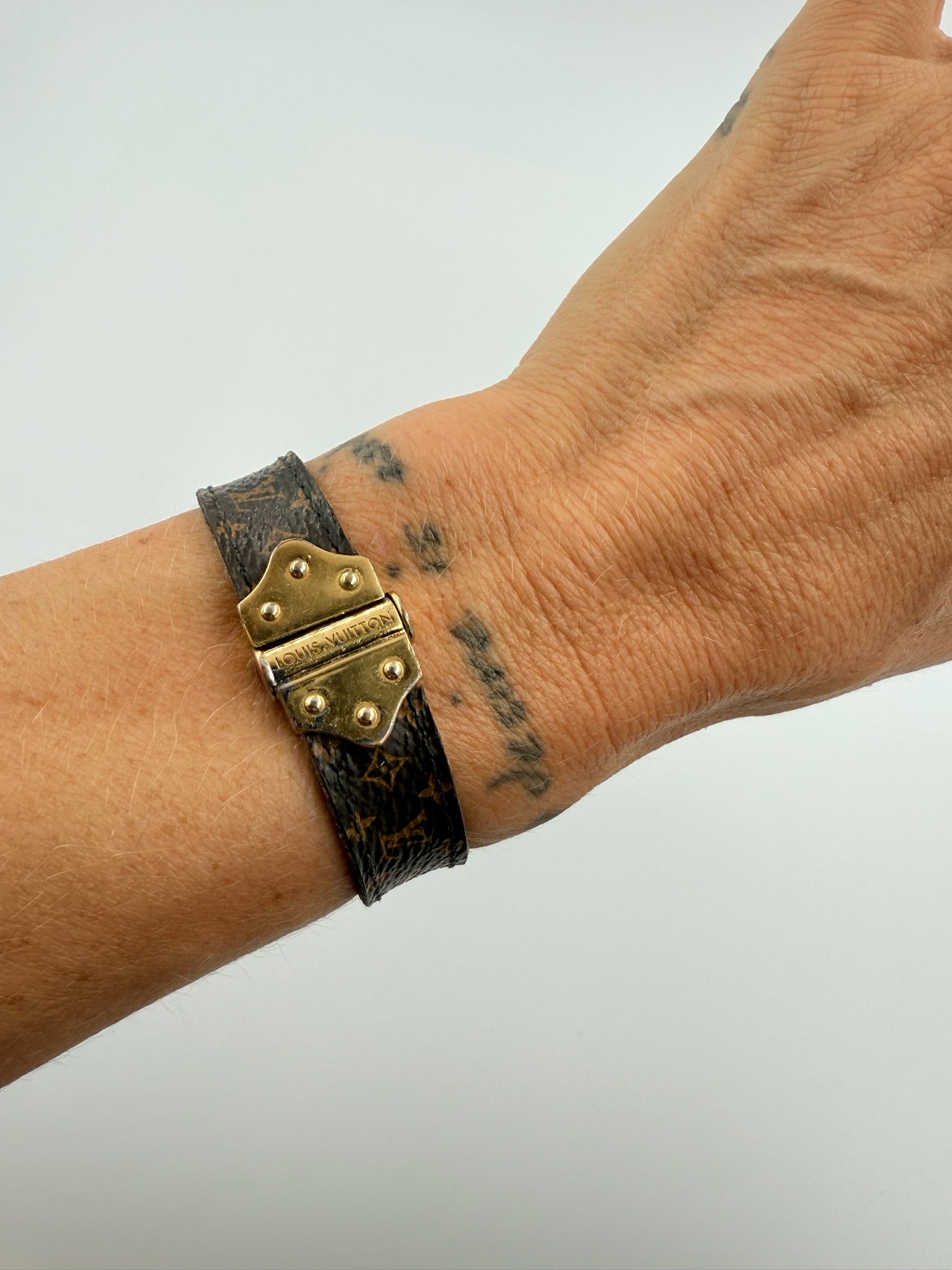 Hånd med Louis Vuitton armbånd, klassisk mønster og guldfarvet spænde.