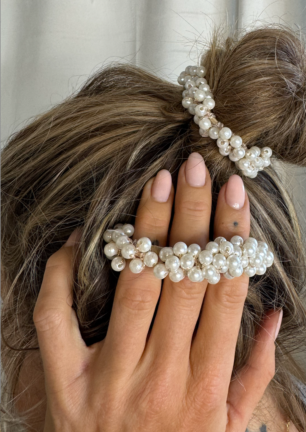 Hår i knold med perle-elastik. Hånd med matchende perle-armbånd hviler på hovedet. Elegant look.