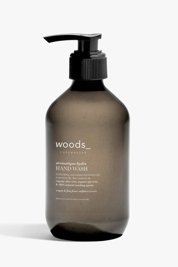 Mørk flaske med pumpe, WOODS Aromatique Hydra Hand Wash, hvid tekst på etiketten.