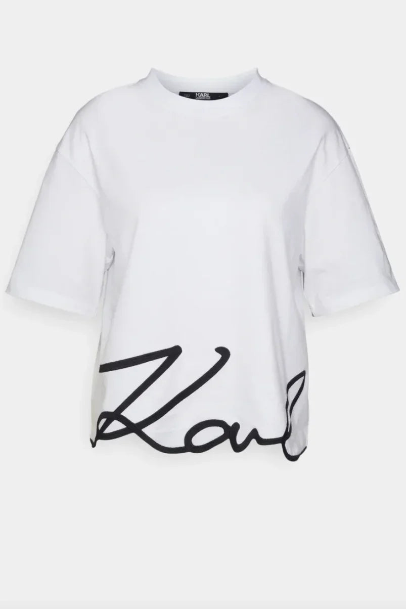 Hvid T-shirt med rund hals og sort, kursiv signatur på kanten.