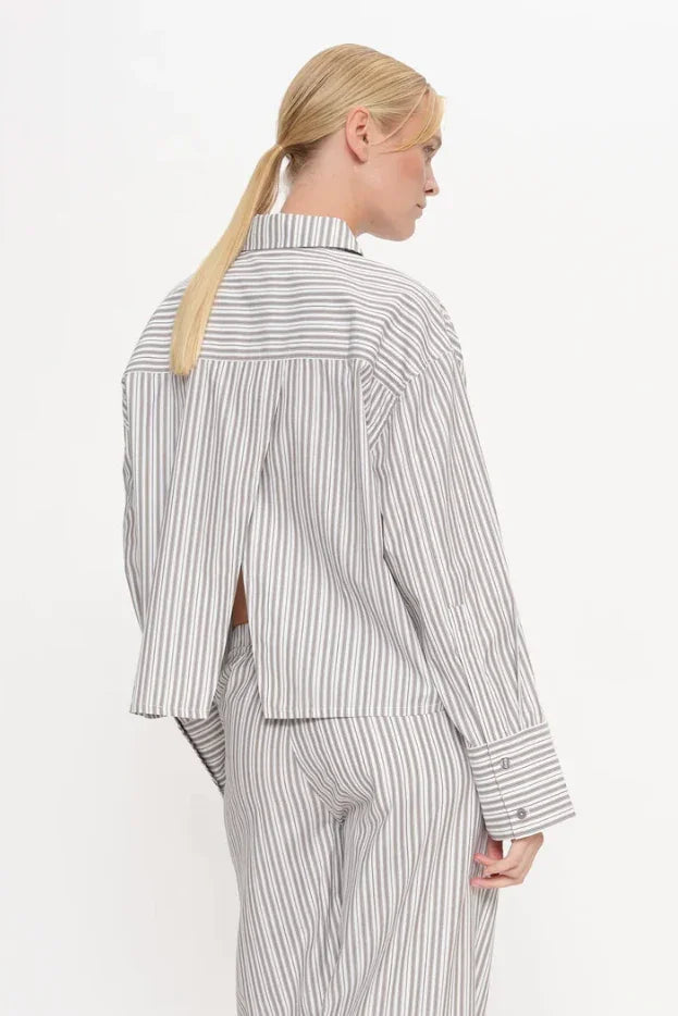 Kvinde bagfra i valnødstribet skjorte med split bagpå, standardkrave og brede ærmer, matchende bukser.