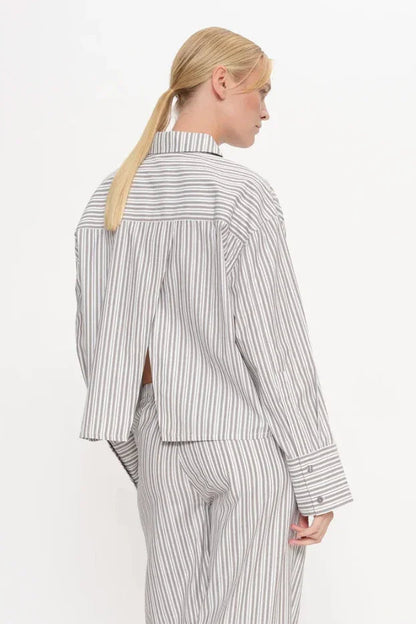 Kvinde bagfra i valnødstribet skjorte med split bagpå, standardkrave og brede ærmer, matchende bukser.