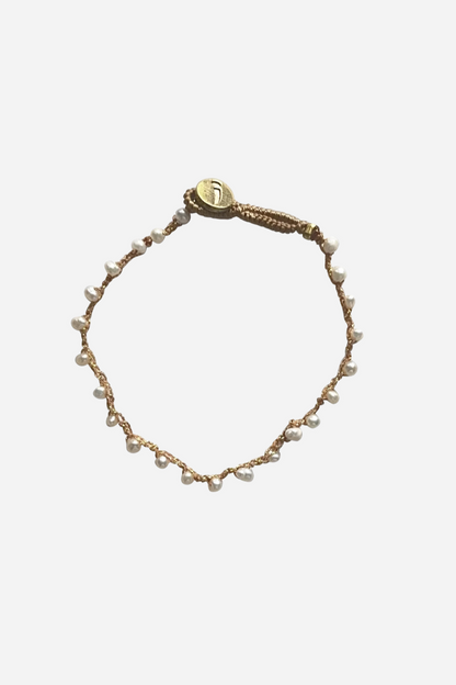 Armbånd med små hvide perler på jordfarvet bånd og rund gylden lukning.