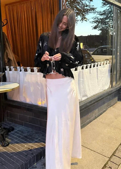 Sort bluse med stjerner og bølget kant, bæres med lys nederdel. Udenfor ved glasdør.