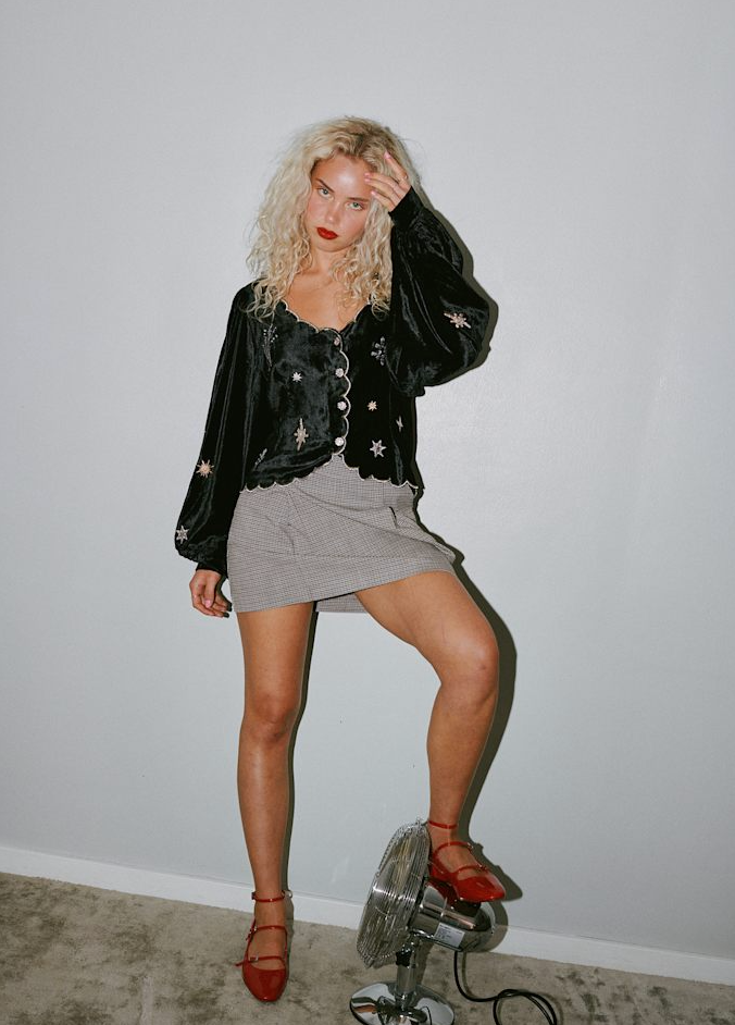 Model i sort bluse med broderede stjerner, bølget kant, knapper, ternet nederdel og røde sko.