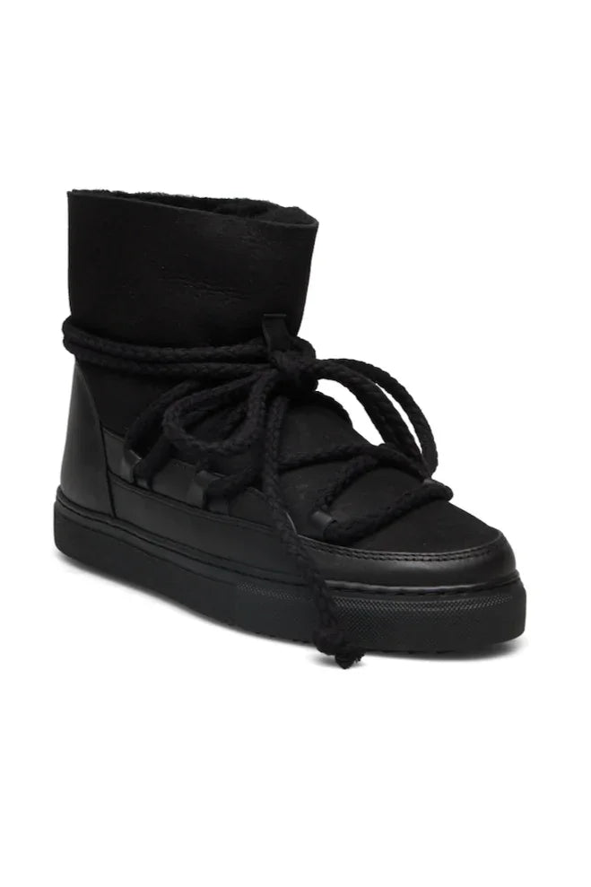 Sort vinterstøvle med højt skaft, tykke snørebånd viklet om og flad, mønstret sål.