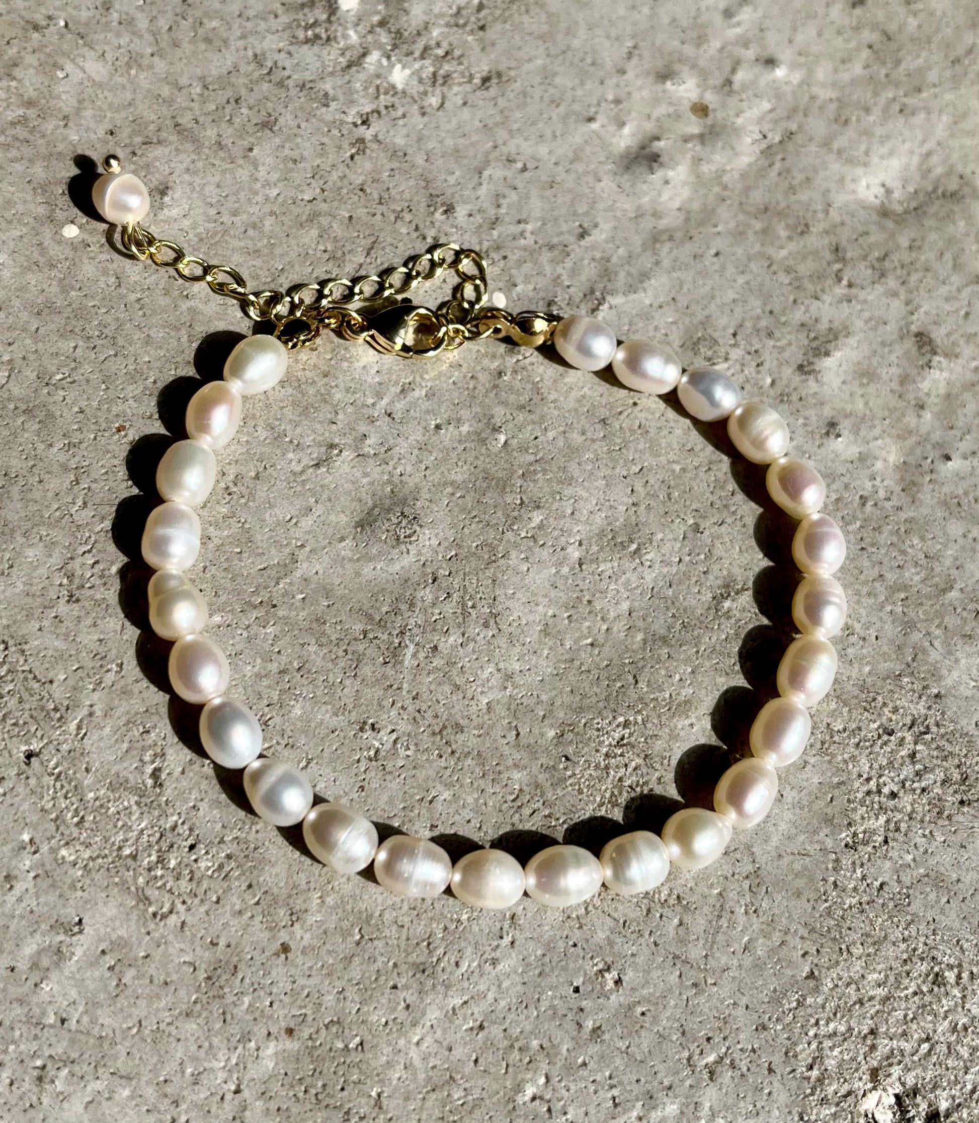 Armbånd med ovale perler i hvide og pastelfarver på en ru overflade. 18 karat guldbelagt kæde.