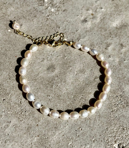 Armbånd med ovale perler i hvide og pastelfarver på en ru overflade. 18 karat guldbelagt kæde.
