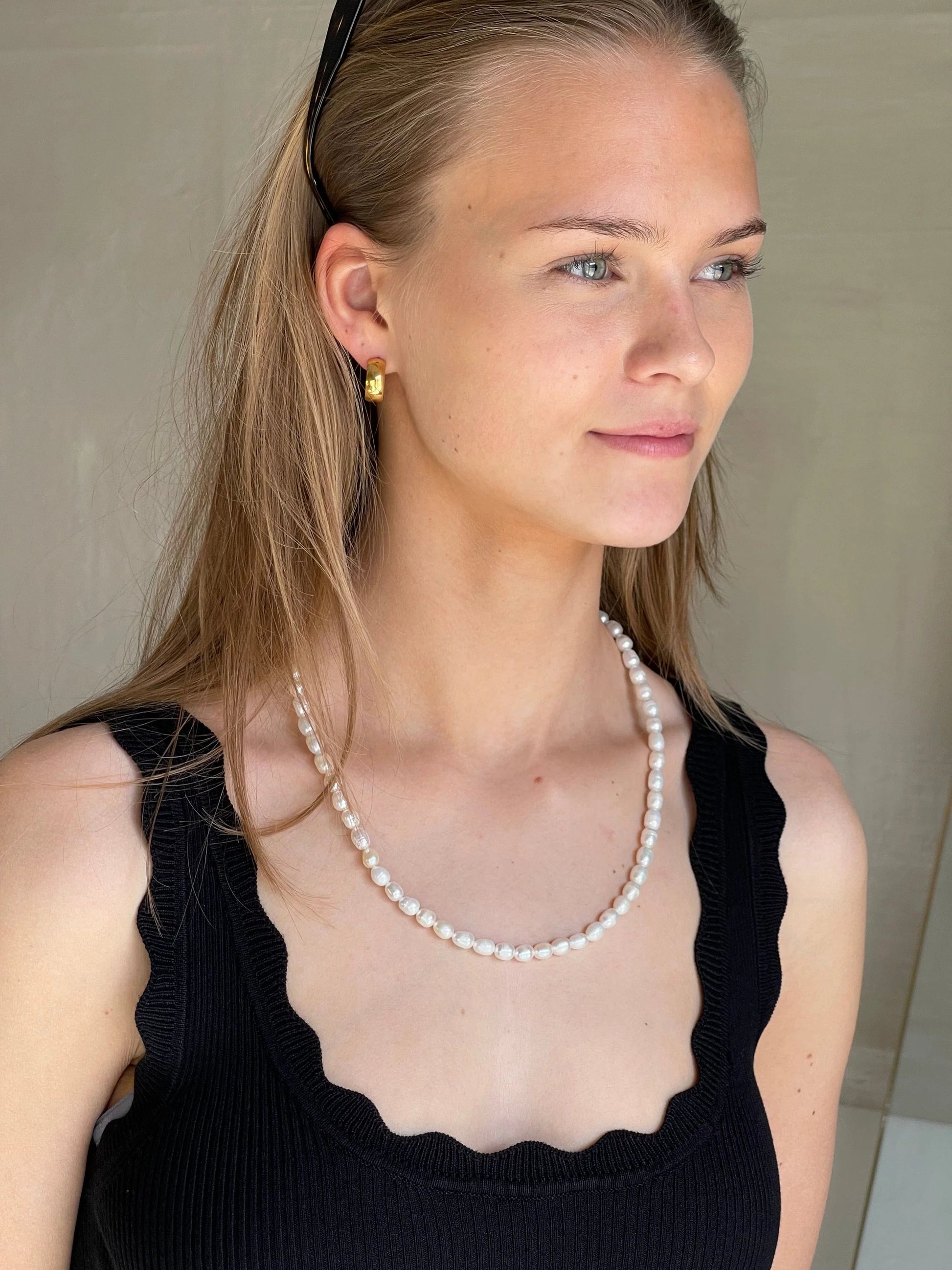 Kvinde med perlehalskæde mod sort top, fremhæver smykkets længde og elegance.