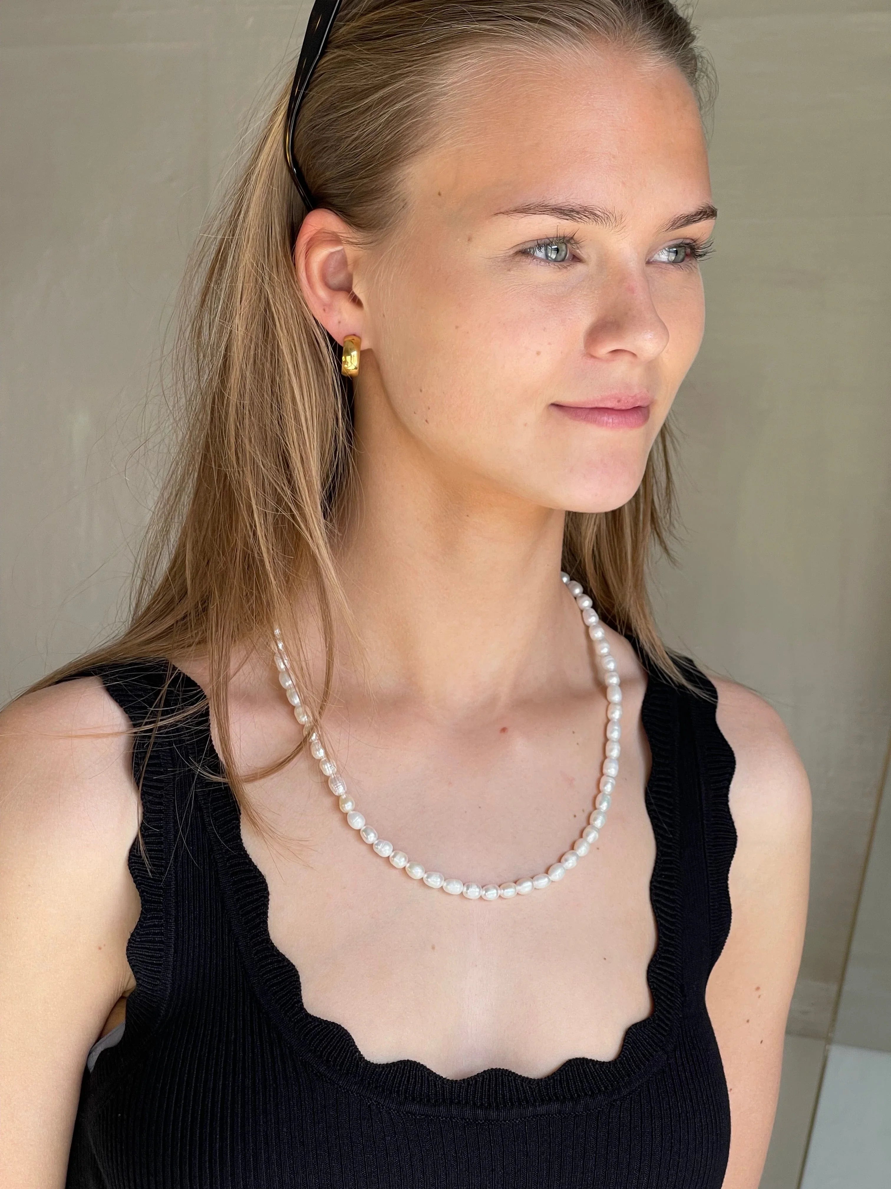Kvinde med perlehalskæde mod sort top, fremhæver smykkets længde og elegance.